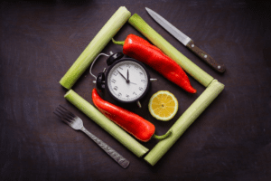 knife and fork arranged around an alarm clock and veggies