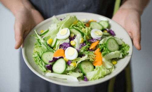 A person holding a bowl of vegetable salad with eggs